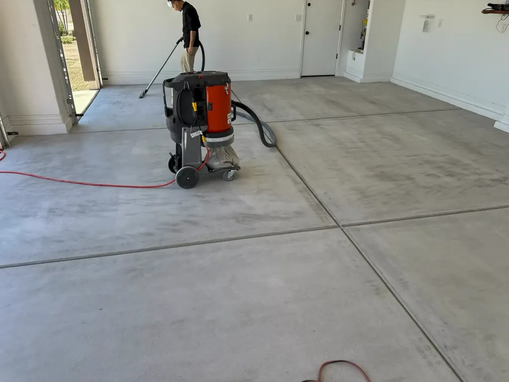 Crew member running a dust-collected concrete grinder across a bare garage slab during surface prep.
