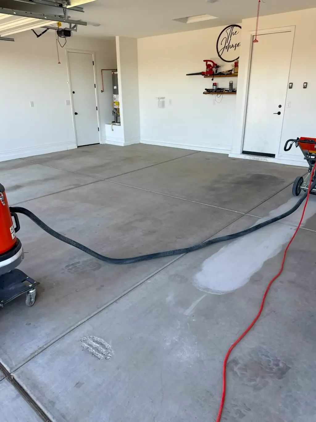 Bare garage slab with grinding equipment and hoses staged before the coating system goes down.