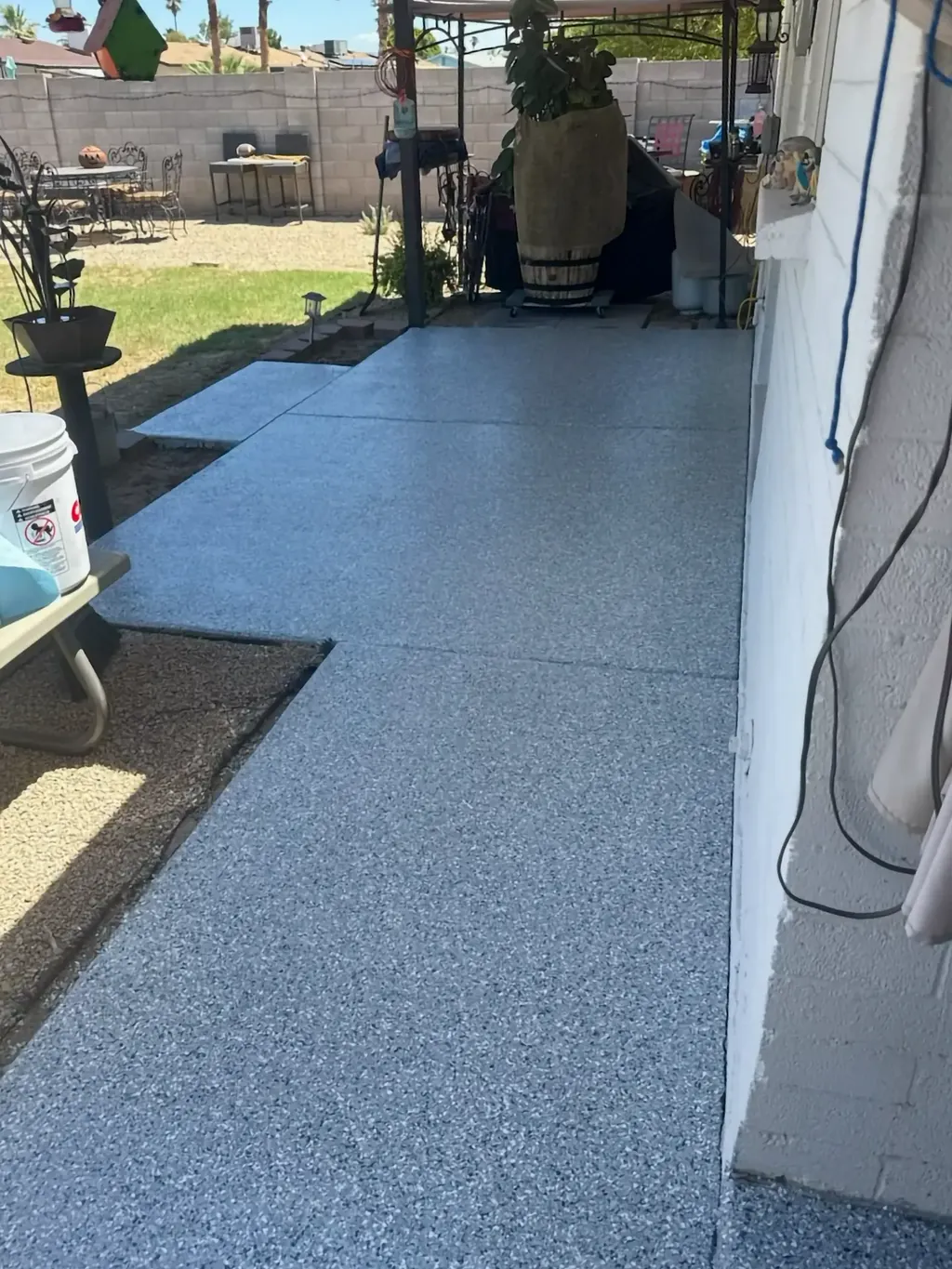Coated concrete patio slab beside a Phoenix-area home, finished with a gray flake broadcast surface.