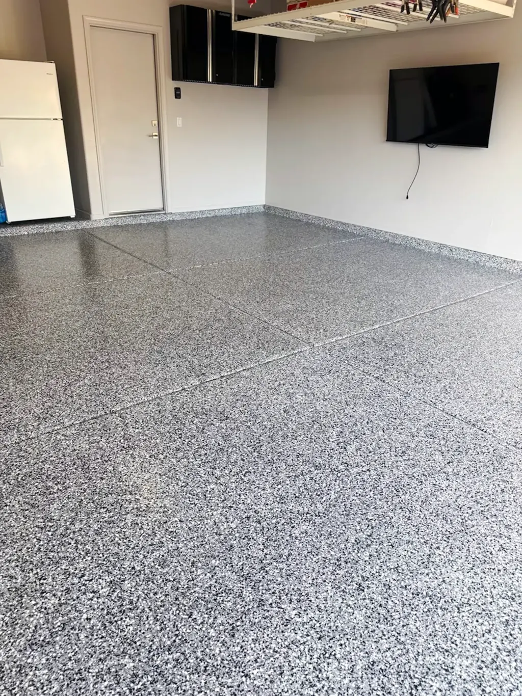 Finished floor coating in a converted garage space with a white and gray flake blend and coated wall base.