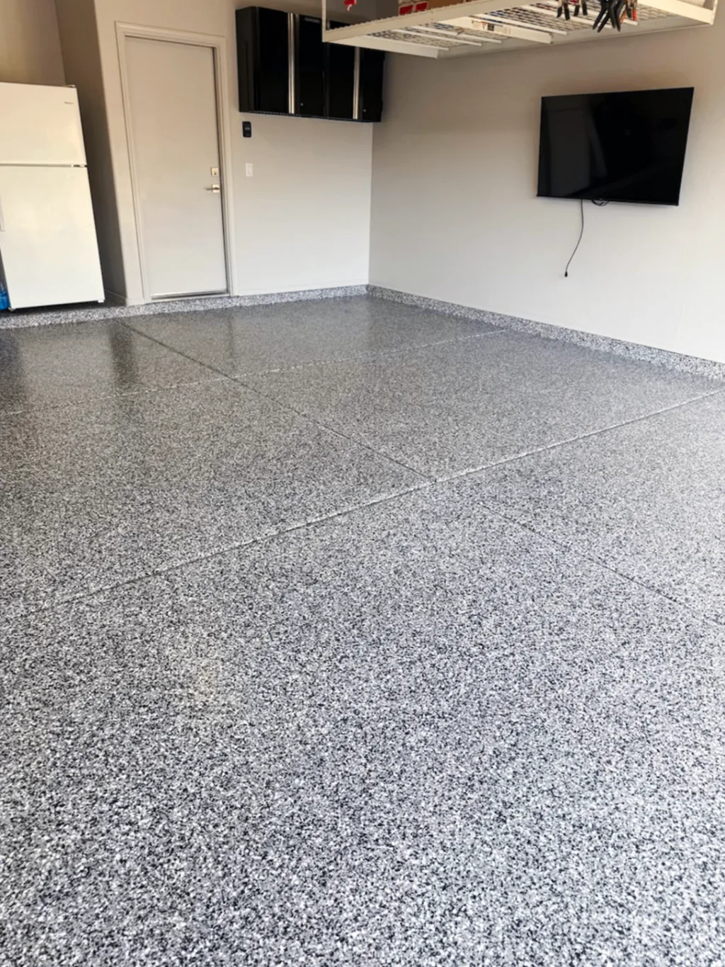 Finished flake floor coating inside a garage, showing a bright polyaspartic topcoat finish and clean perimeter detail.
